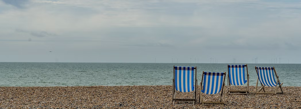 Image of a beach with four blue and white striped deckchairs